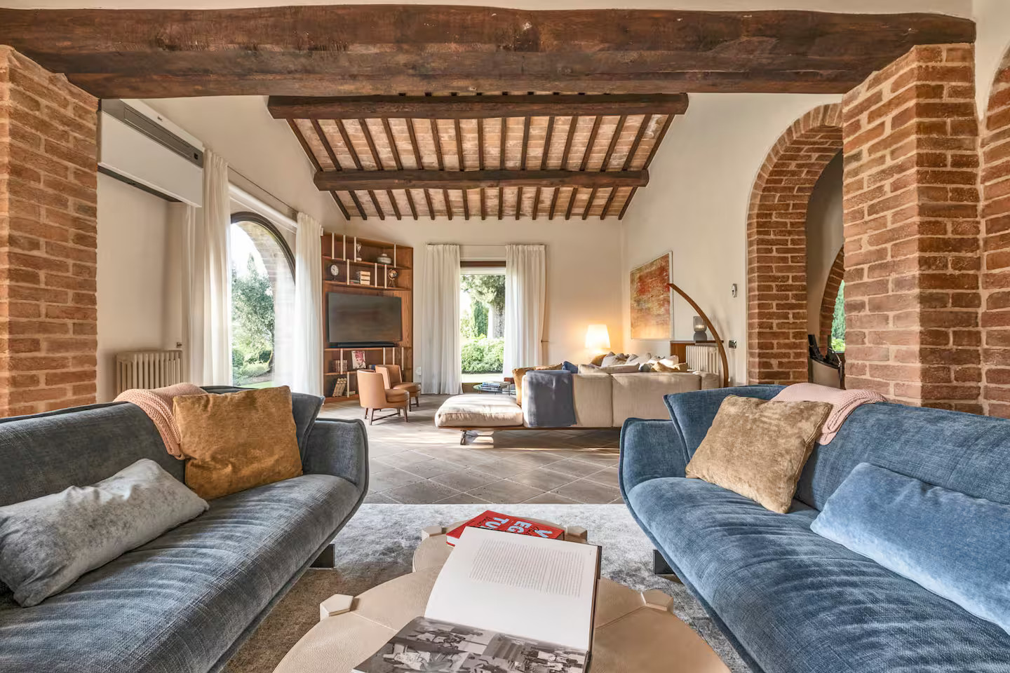 salon murs briques, poutres et fenêtre cintrée maison en pierres Toscane Italie